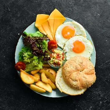 Breakfast. Scrambled eggs, bun, cheese, salad and sauce. On a black stone b.. Stock Photos