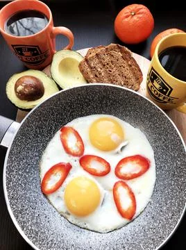 Breakfast of scrambled eggs with pepper and coffee, avocado and tangerine on Foto stock