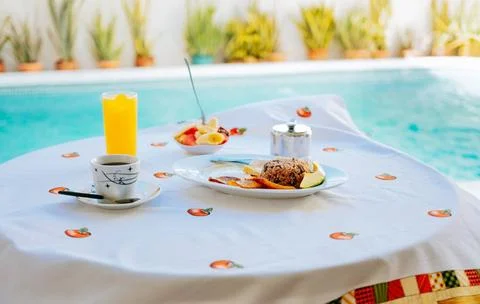 Breakfast served on the table with a swimming pool in the background. frui... Stock Photos