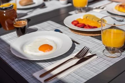 Breakfast is served on top of a table, with an egg on a plate, fruit, orange Stock Photos