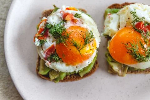 Breakfast served of two toasts with avocado, fried eggs with vegetables and h Stock Photos