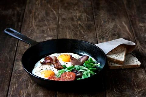 Breakfast set. Pan of fried eggs with bacon, tomato, sage and bread Stock Photos