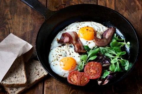 Breakfast set. Pan of fried eggs with bacon, fresh tomato, sage and bread Stock Photos
