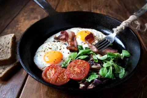 Breakfast set. Pan of fried eggs with bacon, tomato, sage and bread Foto stock