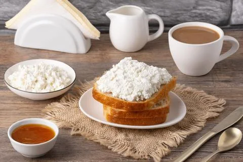 Breakfast setup with bread, cottage cheese, coffee, and jam on a wooden tab.. Foto stock