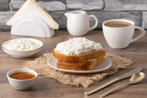 Breakfast setup with bread, cottage cheese, coffee, and jam on a wooden tab.. Foto stock