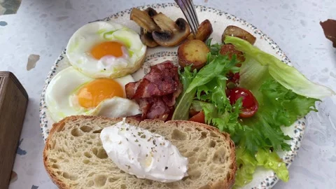 Breakfast spread with fried eggs, bacon, and vegetables on a plate in a cozy set Stock Footage 327530461