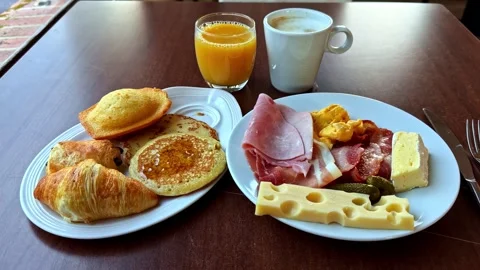 Breakfast spread with pastries coffee orange juice eggs and cold cuts on table Stock Footage 333502860