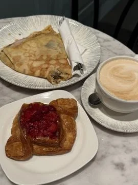 Breakfast table with a crepe, a raspberry pastry, and a cup of cappuccino Stock Photos