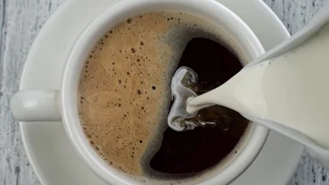 Breakfast time - adding milk to black coffee with foam. Pouring milk into coffee Video stock 223845523