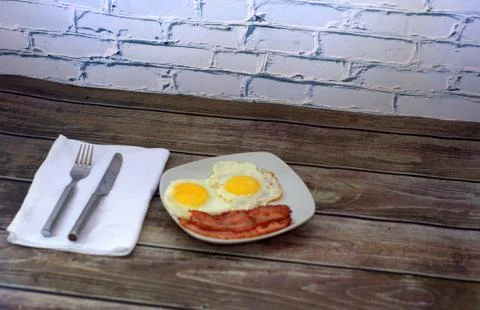 Breakfast, two fried eggs and slices of bacon on a plate, a fork and a knife Stock Photos