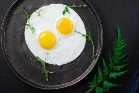 Breakfast with two fried eggs and herbs on black background Stock Photos