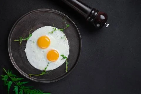 Breakfast with two fried eggs and herbs on black background Stock Photos