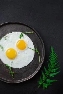 Breakfast with two fried eggs and herbs on black background Stock Photos