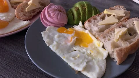 Breakfast on two plates. fried eggs, bread and butter, avocado and sausage Stock Footage 134475006