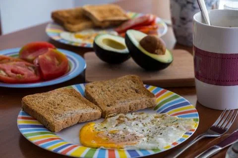 Breakfast wooden table with bread slice, fried egg, tomato and avocado Stock Photos