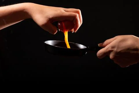 Breaking egg with one hand, isolated on black background. Pouring egg on frying Stock Photos