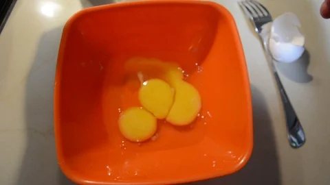 Breaking eggs in a orange plastic bowl. Fresh organic eggs falling into bowl. Pr Vidéo 113817358