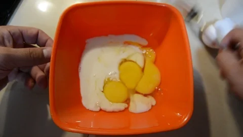 Breaking eggs in a orange plastic bowl. Fresh organic eggs falling into bowl. Pr Stock Footage 113818074