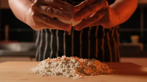 Breaking eggs into a pool of flour to make dough Stock Footage 247728747