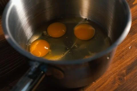 Breaking eggs in pot, raw eggs for beating. Stock Photos