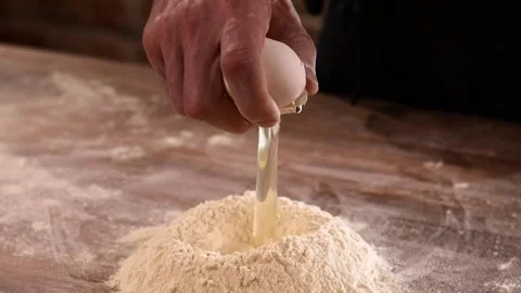 Breaking an fresh egg to a bunch of flour. Dough preparing process Video stock 148728054