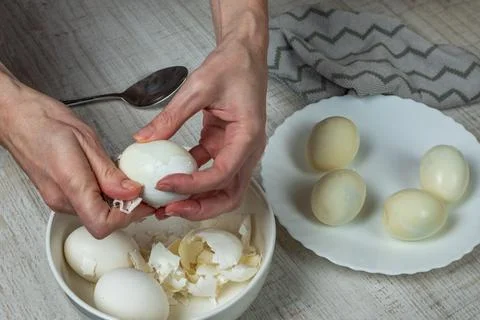 Breaking the shell of a boiled white egg with an iron spoon. Removing the s.. Stock-Fotos