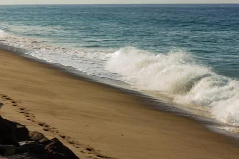 Breaking wave on sandy beach, with backwash, footprints and rocks Stock-Fotos