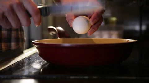 Breaks an egg with a knife above a frying pan for cooking scrambled eggs Stock Footage 86160572
