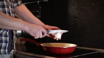Breaks an egg with a knife above a frying pan for cooking scrambled eggs Stock Footage 86160702