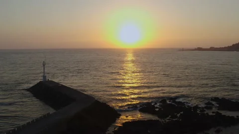 A breakwater and a small lighthouse at sunset. A drone flying towards the sun. Stock Footage 138692524