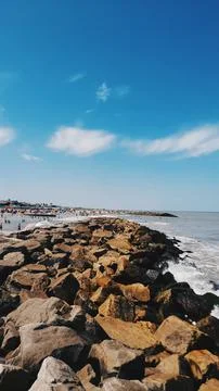 Breakwater, beach, rocks, sky with clouds, sea, waves Stock Photos