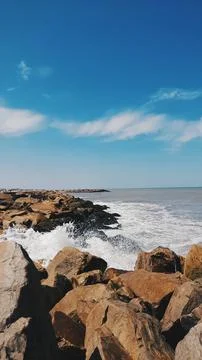 Breakwater, beach, rocks, sky with clouds, sea, waves Stock Photos