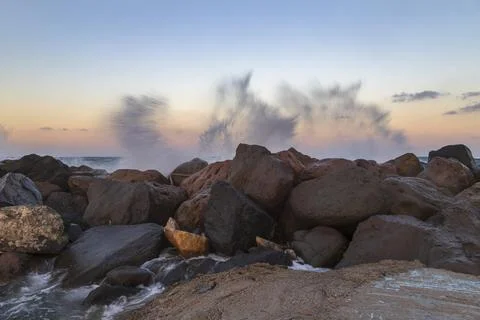 Breakwater made of stone into which waves crash. Background is blue sky at .. Stock Photos