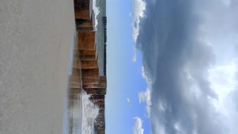 Breakwater view on the sandy beach and cloud sky in the background. Stock Photos