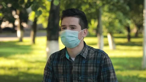 Breathing without mask. Young man stands in the city park, takes off the Vídeos de archivo 136387362