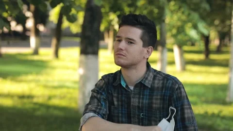Breathing without mask. Young man stands in the city park, takes off the Stock Footage 140132686