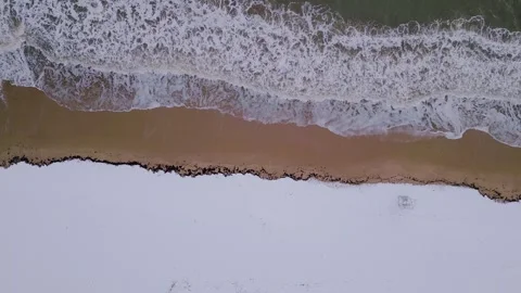 A breathtaking aerial view of ocean waves crashing onto a snow-covered beach Stock Footage 302443258