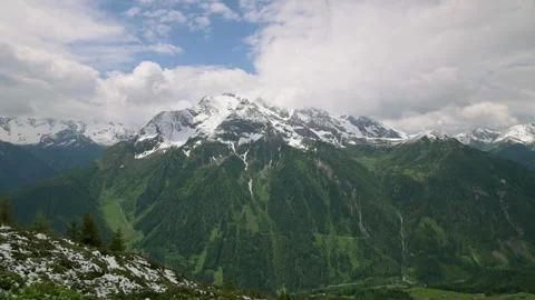 A breathtaking panoramic view of snow-capped mountains and lush green valleys in Vídeo Stock 282205237