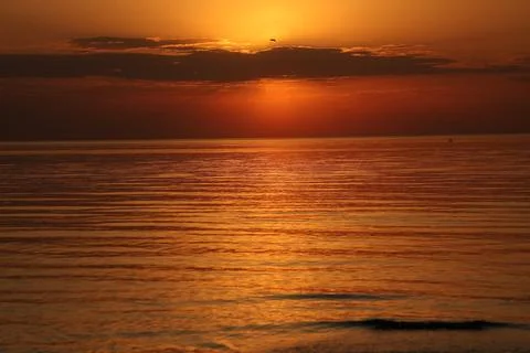 Breathtaking seascape during a warm orange sunset. A bright sun peeks through Stock Photos