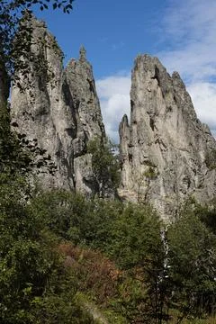 Breathtaking sharp high grey cliff with jagged peaks, cracks surrounded green Stock Photos