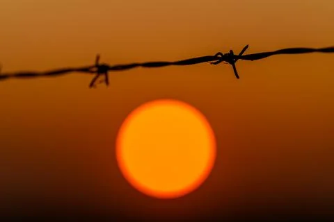 The breathtaking sunset behind barbed wire serves as a powerful symbol of both i Stock Photos