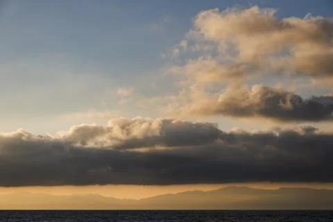 Breathtaking sunset over the ocean with dramatic clouds and distant mountains Photos