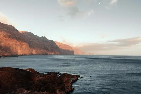 Breathtaking sunset view of rugged cliffs Los Gigantes meeting calm ocean waters Stock Photos