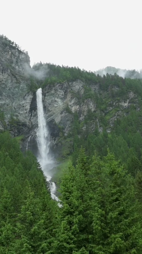 A breathtaking vertical view of a tall waterfall cascading down the forested Stock Footage 287318401