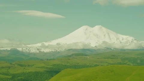 A breathtaking view shows a large snow-covered mountain surrounded by lush green Stockbeeldmateriaal 312516653
