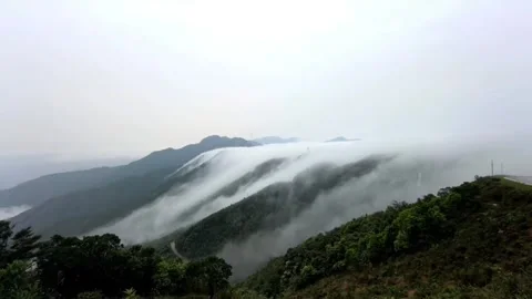 A breathtaking view of thick clouds cascading over lush green mountain ridges in Vídeos de archivo 334163531