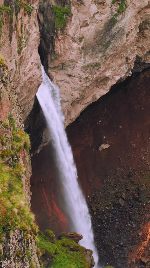 A breathtaking waterfall flows forcefully down rugged cliffs surrounded by lush Stock Footage 312464000