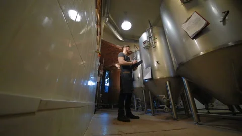 The brewer on the background of beer tanks makes calculations Stock Footage 100521884