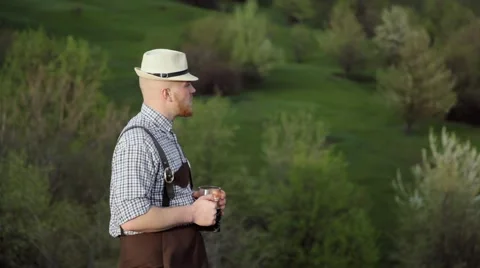 Brewer standing against a background of green hills enjoying dark beer. Stock Footage 63196723